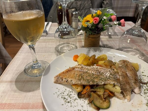 ドブロニクのRestoran Lajkで提供された魚料理と白ワインのグラス。長期間放置され酸化したような味のワイン。