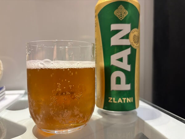 ホテルの部屋のテーブルに置かれた、Pan Zlatniの缶とグラスに注がれた美しい黄金色のプレミアムラガービール