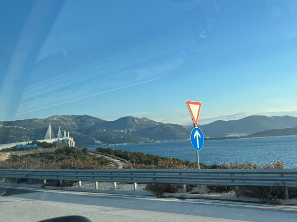 冬の澄んだ青空の下、ミニバンの車窓から見えるペレシャツ橋と美しい海岸線の景色。ボスニア国境へと向かう道中の風景。
