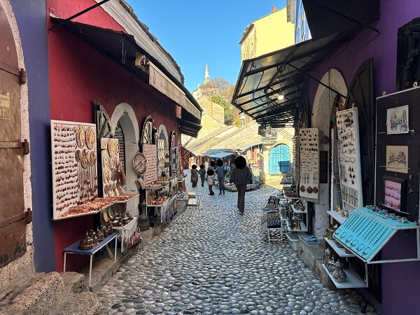 冬のモスタル旧市街にあるバザール(市場)の通り。丸い石畳の路地の両側に、銅細工やアクセサリーなどの色鮮やかなお土産が並んでいる風景。