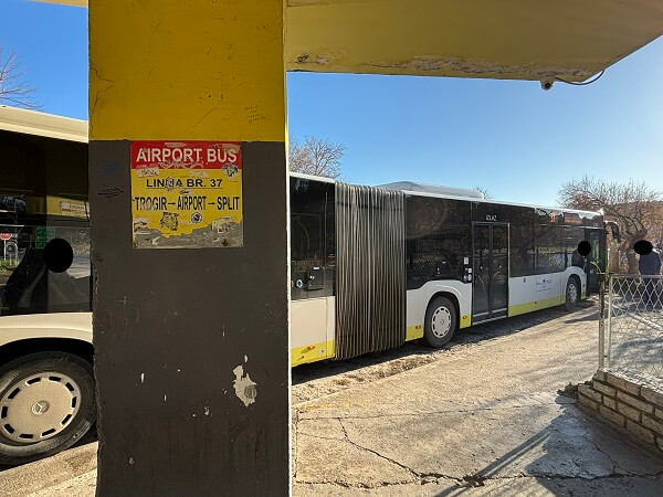 スプリトの37番バス乗り場の柱にあるAIRPORT BUS LIN IJA BR. 37の黄色い看板と背景の連節バス。