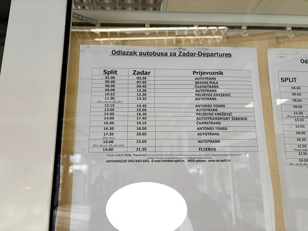 スプリトバスターミナルの窓口ガラスに貼られた、ザダル行きのバス時刻表。紙には「Odlazak autobusa za Zadar-Departures」と書かれ、出発時刻、到着時刻、バス会社名(BRIONI PULA、FLIXBUSなど)がリスト化されている。