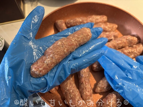 青いゴム手袋をはめた手で棒状に丸めた肉だねを持っている様子